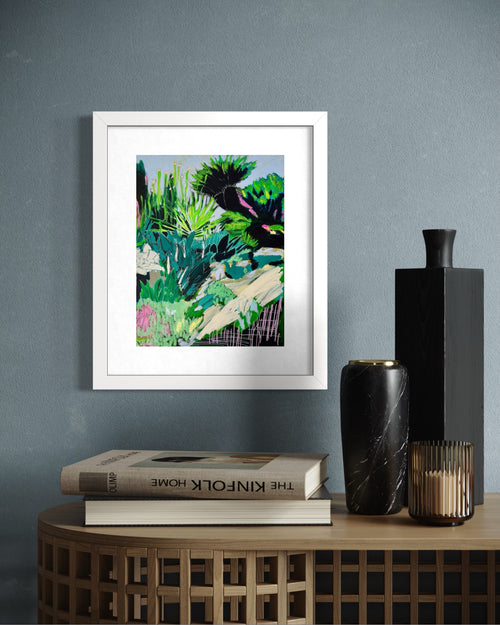 Framed limited edition print of an abstract garden landscape on a wall above books and decorative vases.