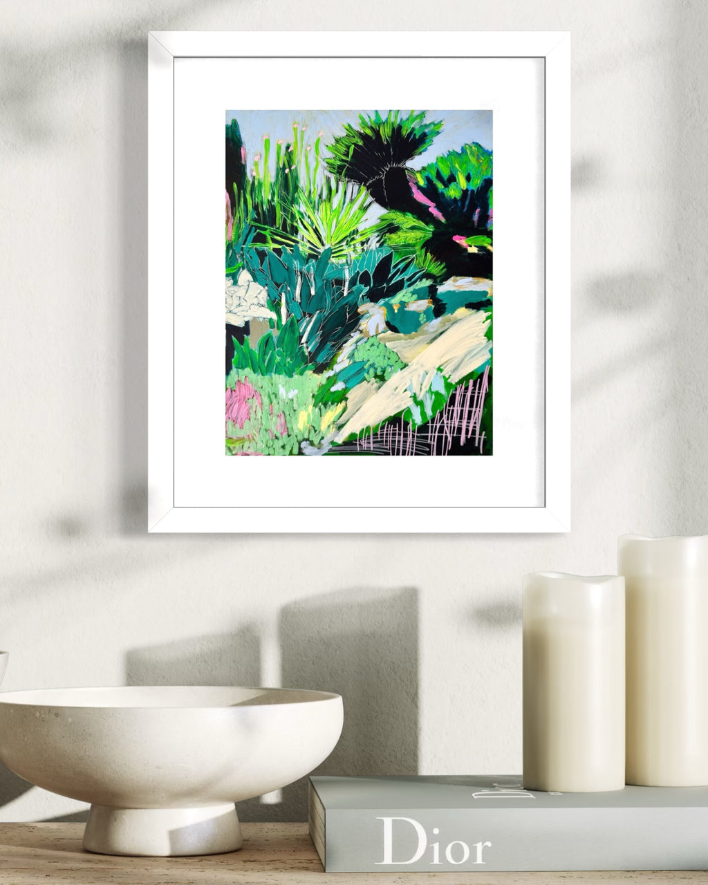 Framed abstract limited edition print with vibrant colours on a wall above a shelf with a Dior book. 