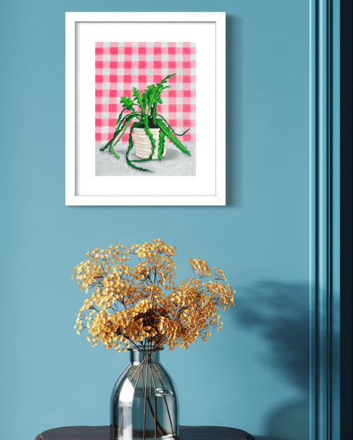 Framed limited edition print of a plant on a pink checkered background above a vase with dried flowers on a blue wall.