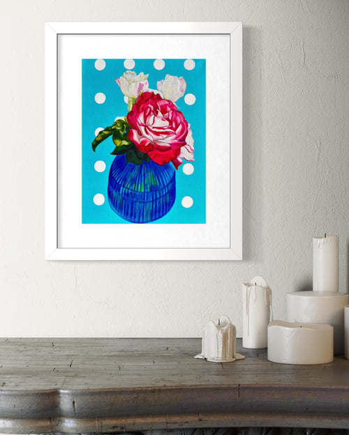 Framed limited edition print of a colourful flower arrangement on a polka dot background, displayed on a wall above a wooden surface.