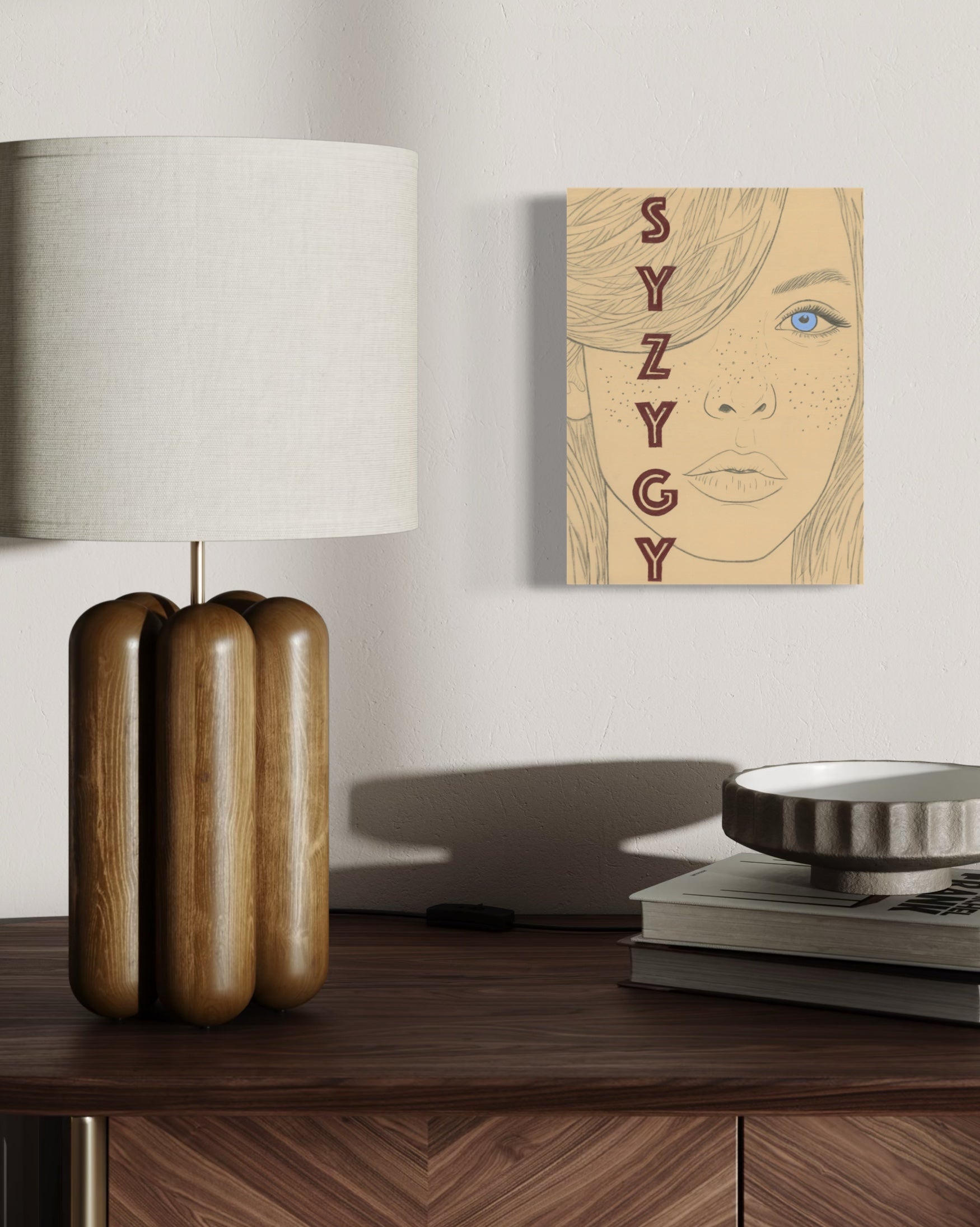 Decorative lamp and original painting on board with a neutral background.  The painting is an illustration of a woman's face with 'SYZYGY' text overlay on a beige background.