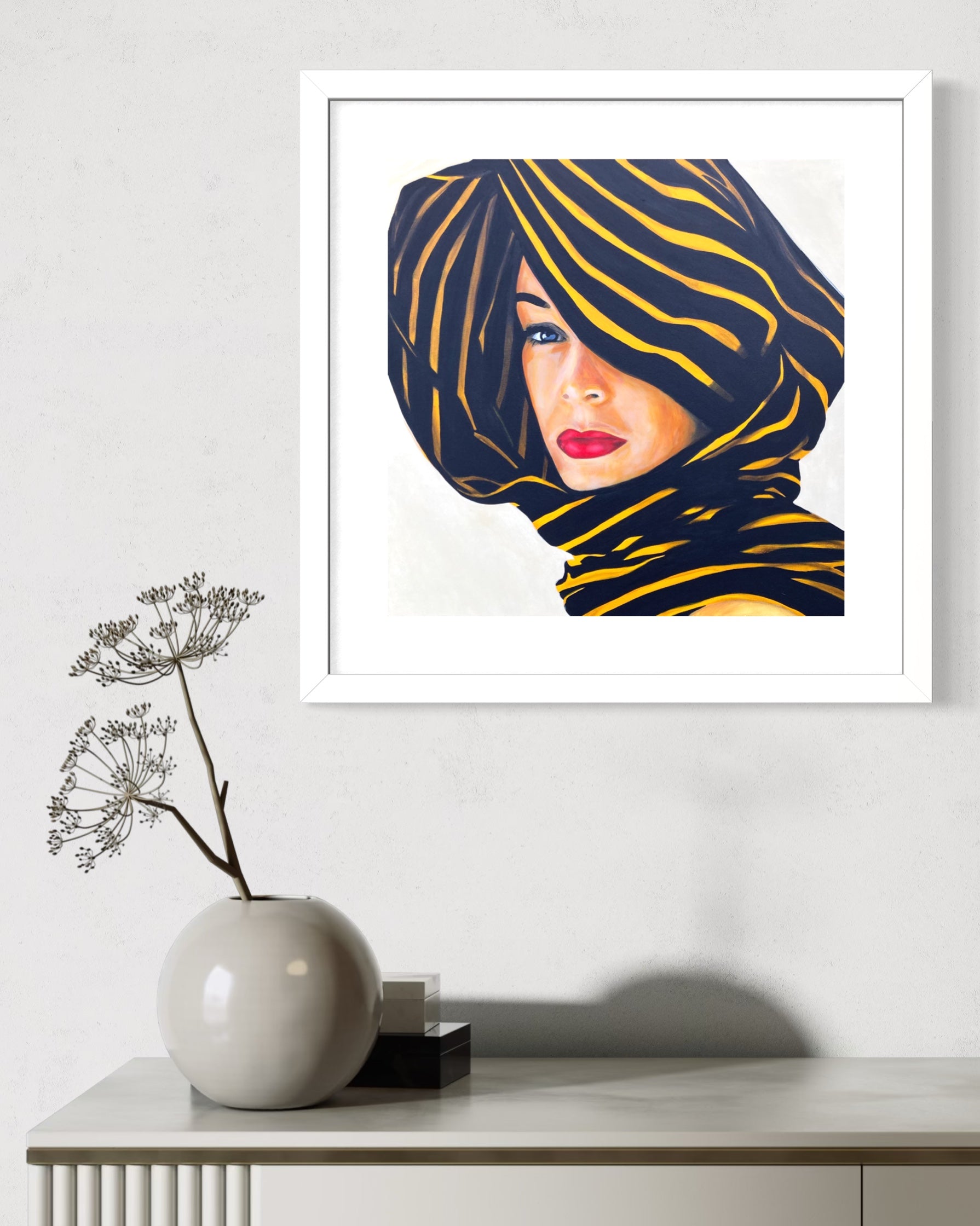 Framed limited edition print of a woman wearing a zebra-striped headscarf on a white wall above a table with decorative items.