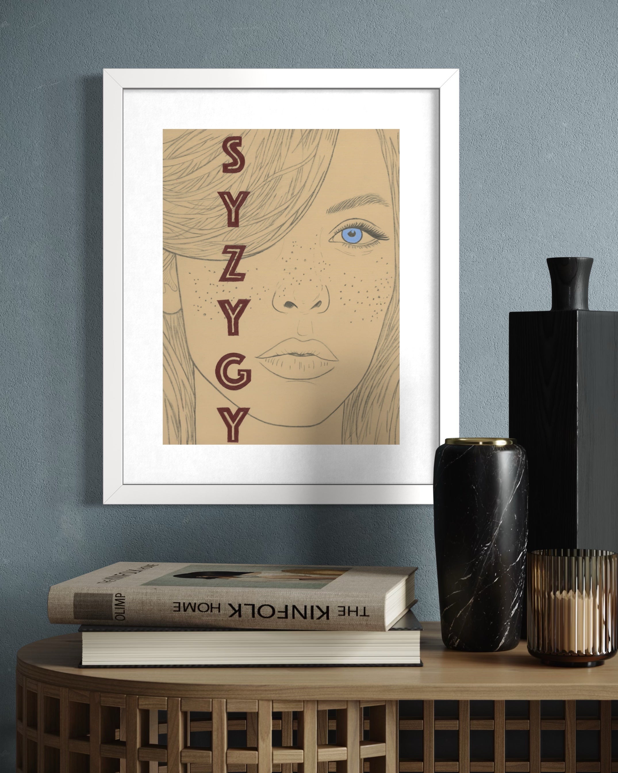 Framed limited edition print with 'SYZYGY' design on a wall above books and decorative items.