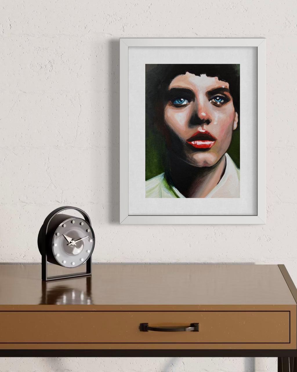 A framed portrait painting of a woman with dark hair, blue eyes, and red lips, displayed on a textured white wall above a brown wooden console table with a black clock.