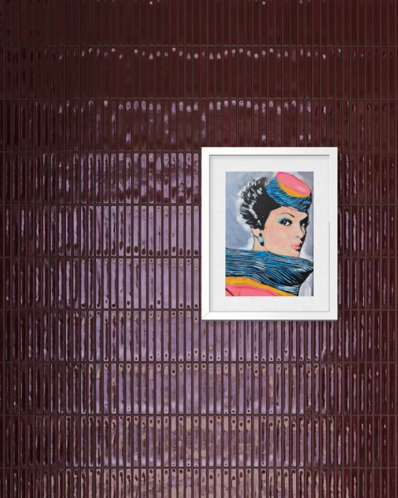 A framed art print featuring a stylized portrait of a woman with a pink hat and blue scarf, mounted on a dark brown ribbed metal wall.