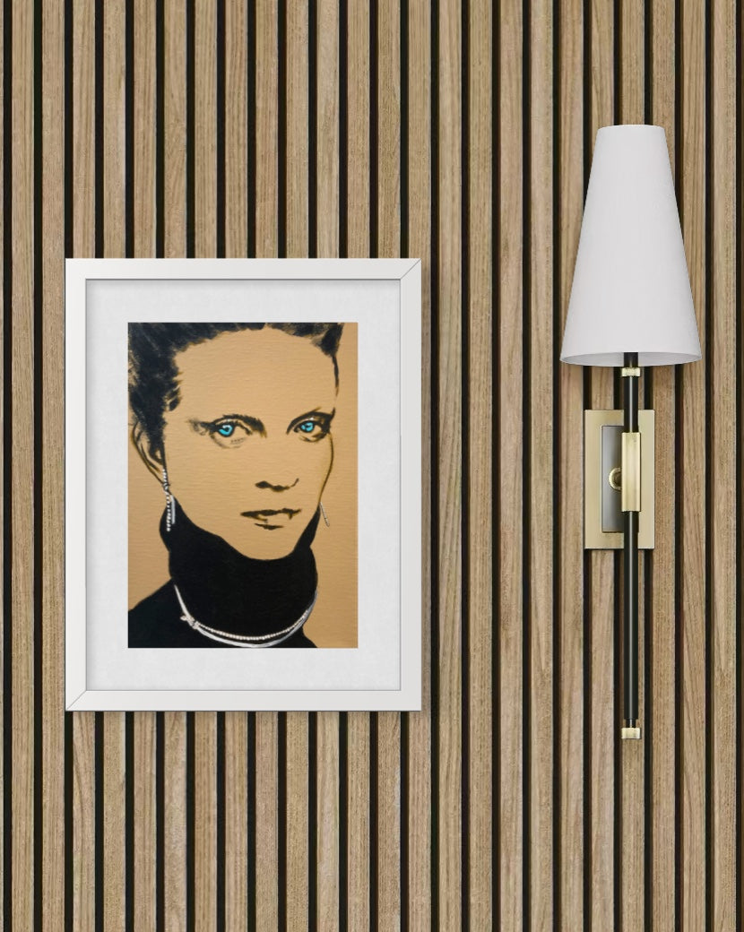 A framed pop-art portrait print of a woman with blue eyes, displayed on a wood slat wall next to a modern wall sconce.