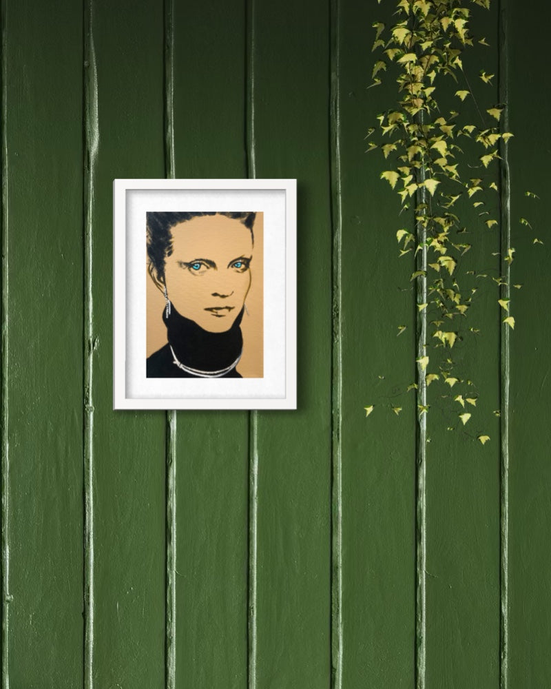 A framed pop-art portrait print of a woman with blue eyes, displayed on a dark green wooden wall with climbing ivy on the right.