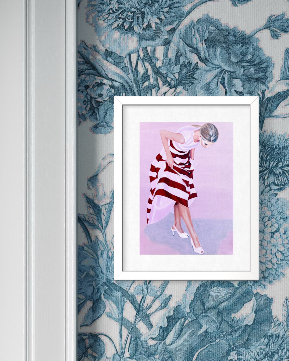 A framed art print featuring a stylized illustration of a woman in a red and white striped dress, displayed on a blue floral wallpaper next to a white door frame.