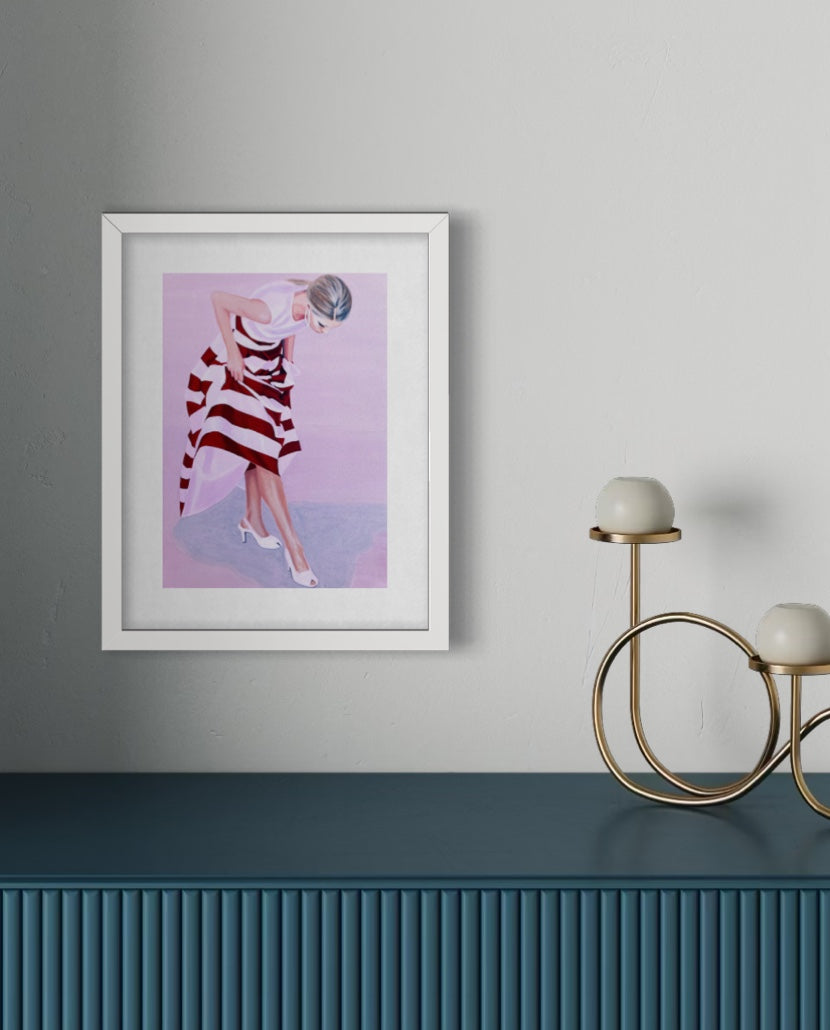 A framed art print featuring a woman in a red and white striped dress against a pink background, displayed on a gray wall above a dark blue ribbed console table with a gold two-light candle holder.