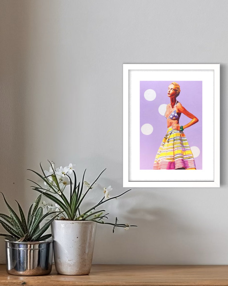 A framed art print featuring a retro-style illustration of a woman in a colorful striped skirt and patterned top against a lavender background, displayed on a light gray wall above a wooden shelf with potted plants.