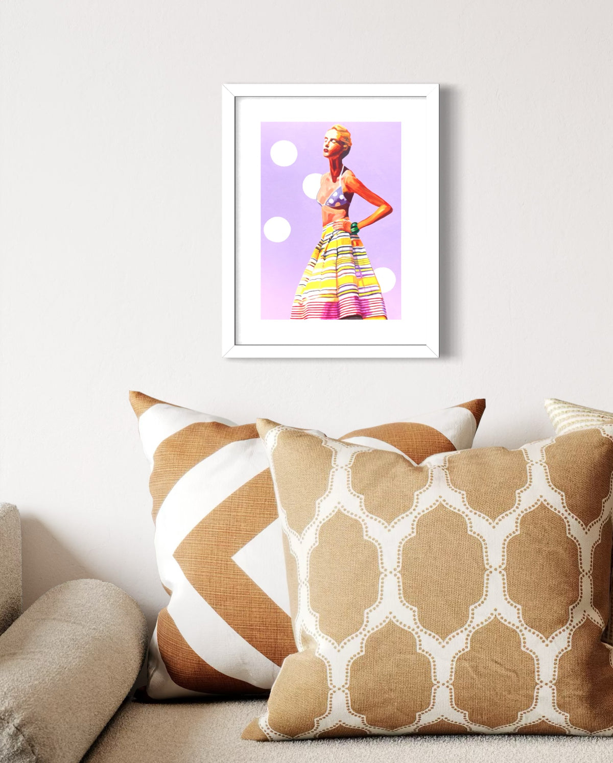 A framed art print featuring a retro-style illustration of a woman in a colorful striped skirt and headband against a lavender background, displayed on a light gray wall above a couch with patterned beige and white pillows.