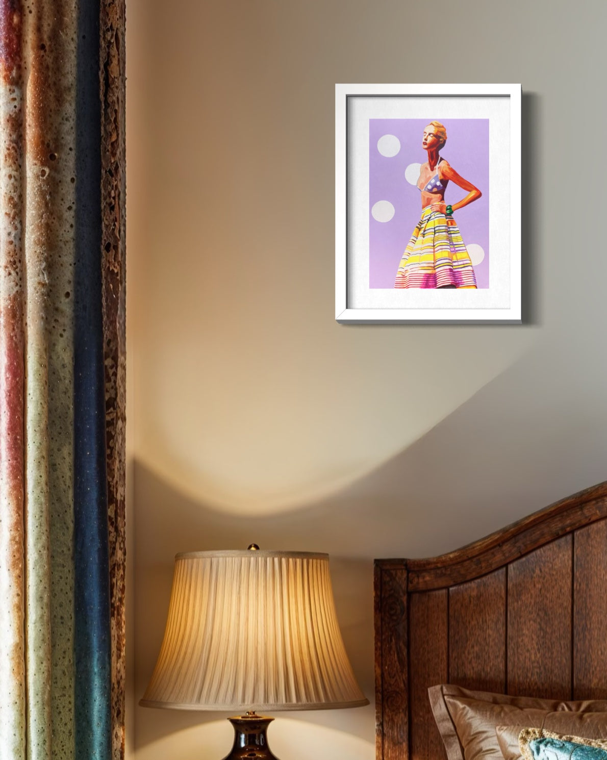 A framed art print featuring a colorful fashion illustration of a woman in a striped skirt against a purple background, displayed on a beige wall above a bed with a lit lamp.