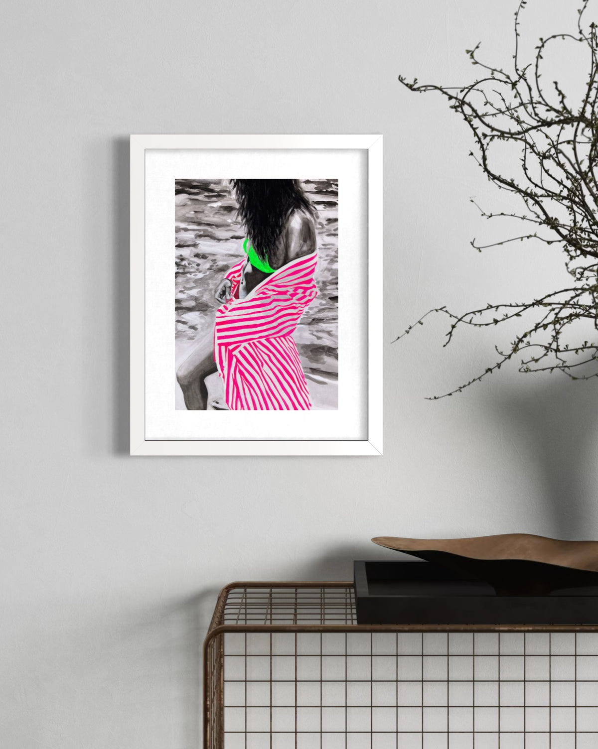 A framed art print featuring a woman in a pink and white striped dress with a bright green bikini top, displayed on a light gray wall above a wire grid side table.