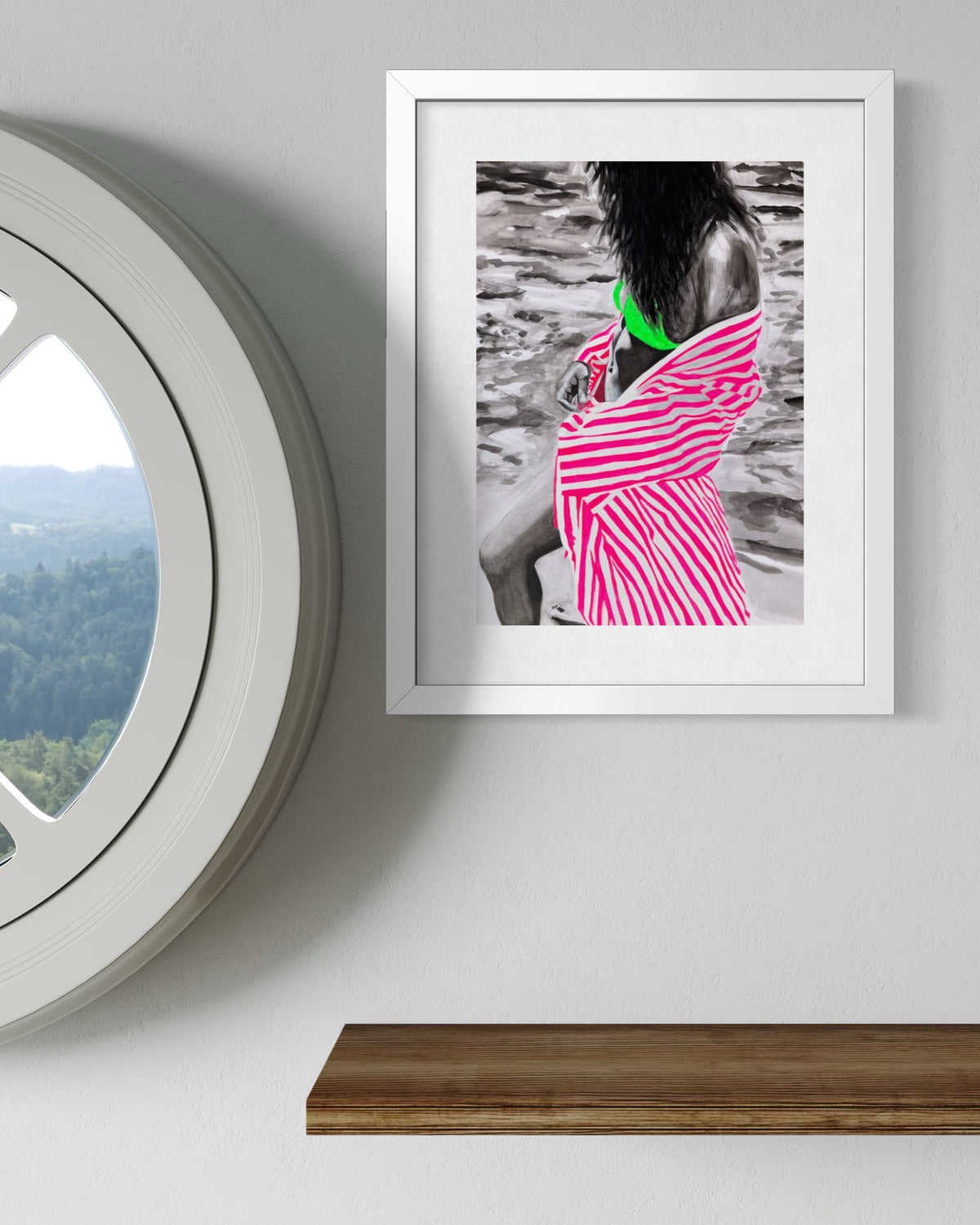 A framed art print hanging on a light gray wall next to a circular window and above a wooden shelf. The print features a black-and-white photo of a woman with vibrant pink and white stripes on her dress and a bright green collar accent.
