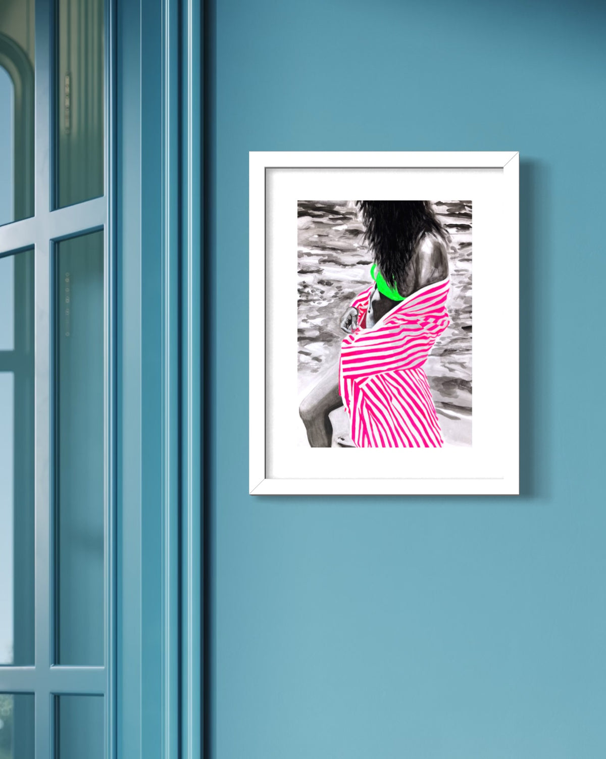 A framed art print featuring a woman wrapped in a pink and white striped cloth, with selective color highlighting her green bikini top, displayed on a blue wall next to a window.