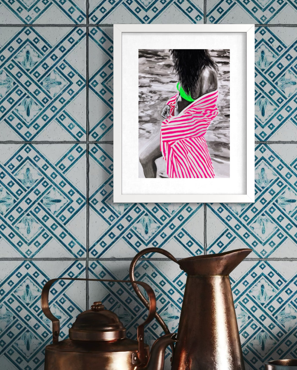 A framed art print featuring a black and white photograph of a woman in a pink and white striped dress with a bright green top, hung on a blue patterned tile wall above vintage copper pots.