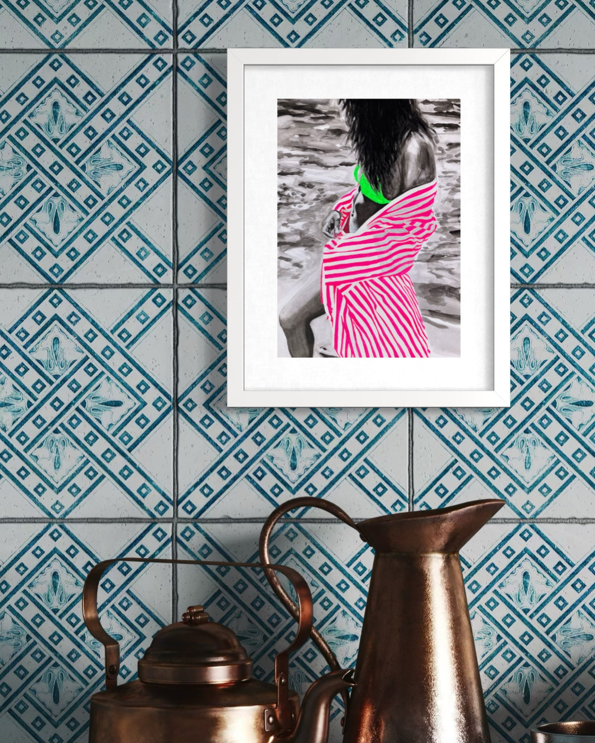 A framed art print featuring a black and white photograph of a woman in a pink and white striped dress with a bright green top, hung on a blue patterned tile wall above vintage copper pots.