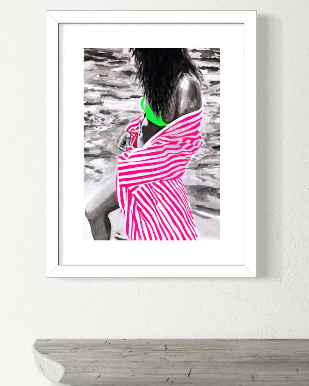A framed art print hanging on a white wall above a gray wooden mantel. The print features a black and white photograph of a woman with a vibrant pink and white striped cover-up and a bright green bikini top highlighted in color.