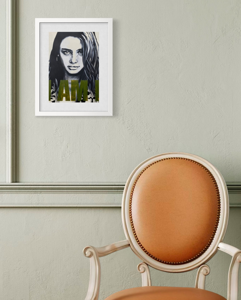 A framed black and white portrait print with olive green text hanging on a textured light green wall above a tan upholstered chair.